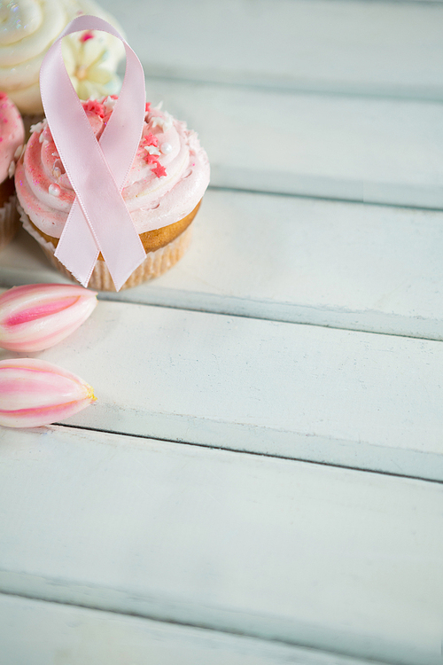 Close-up of Breast Cancer Awareness pink ribbons on cupcakes with tulips over white wooden table