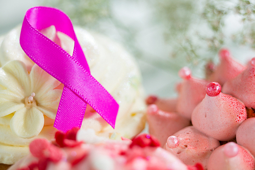 Close-up of pink Breast Cancer Awareness ribbon on cupcake by flower over table