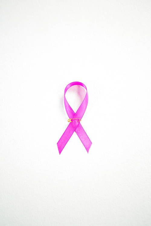 Directly above view of pink Breast Cancer Awareness ribbon with safety pin against white background