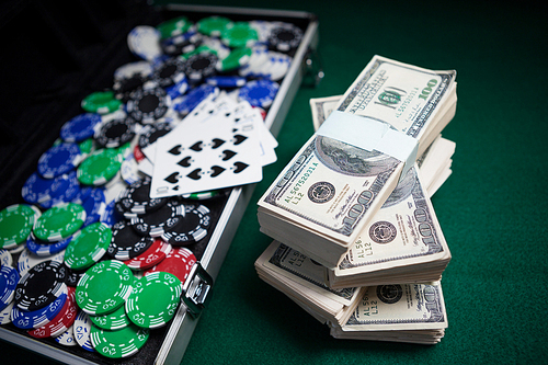 Bundle of US dollars, playing cards and casino chips on poker table in casino