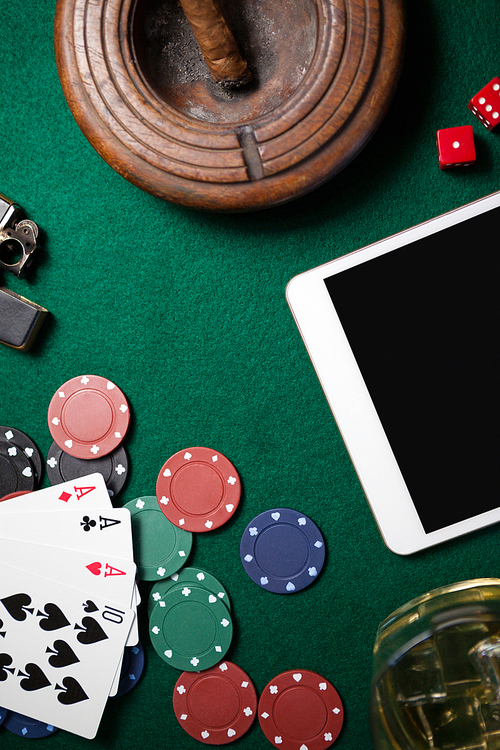 Ashtray, digital tablet, dice, casino chips and playing cards on poker table in casino