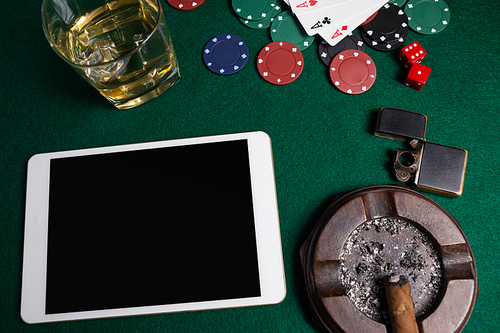 Ashtray, lighter, digital tablet, dice, casino chips and playing cards on poker table in casino