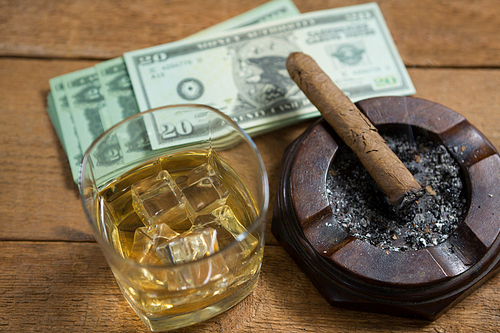 High angle view of whisky and cigar by paper currency on wooden table