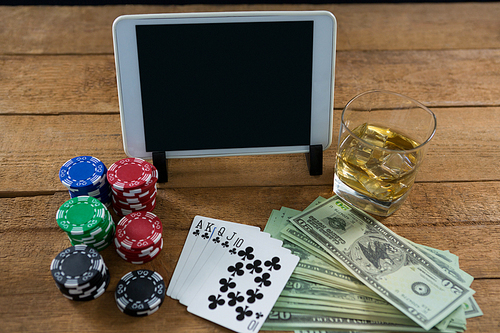 High angle view of digital tablet and whisky with currency on wooden table during poker game at casino