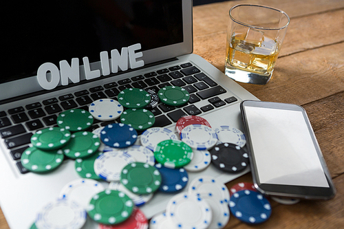 Close-up of scattered chips and aces with technologies on wooden table