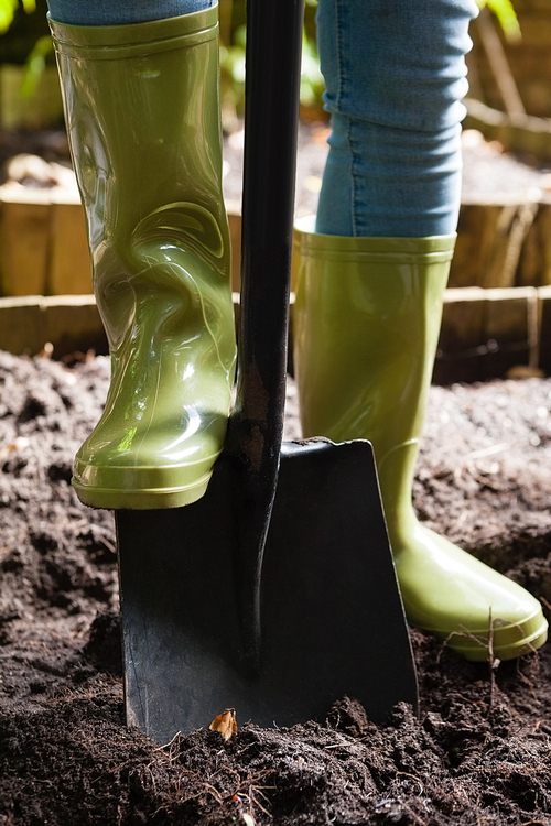 Low section of woman standing with shovel on dirt at backyard