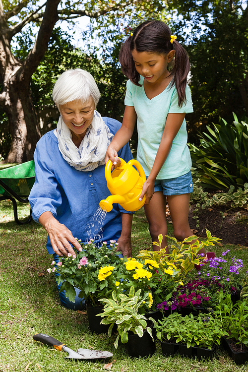 Senior woman looking at girl watering flowers in backyard