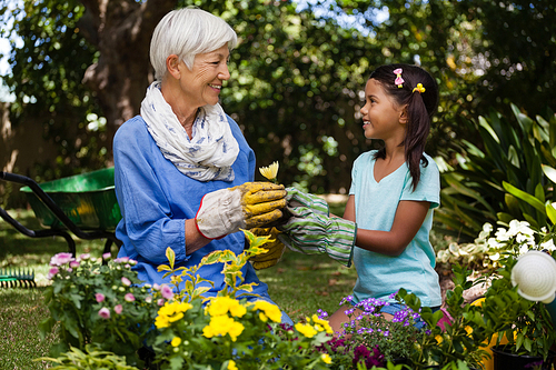 Smiling grandmother and granddaughter looking at each other while holding flower in garden