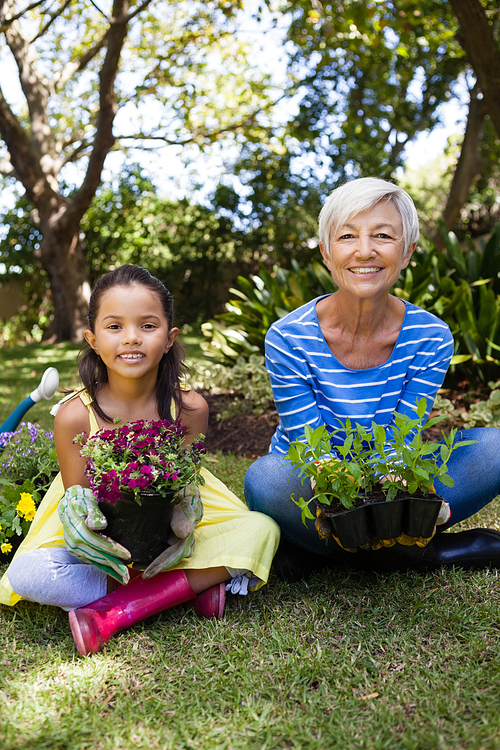 Portrait of smiling granddaughter and grandmother holding plants sitting with crossed legs at backyard