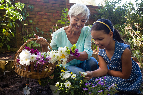 Smiling senior woman carrying flower basket looking at granddaughter while gardening in backyard