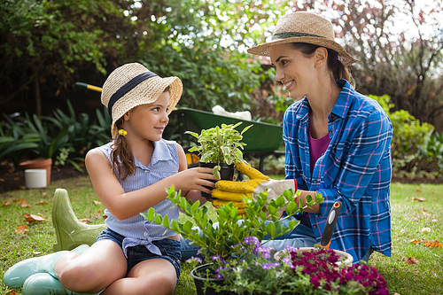 Smiling daughter and mother with potted plants sitting on grass in backyard