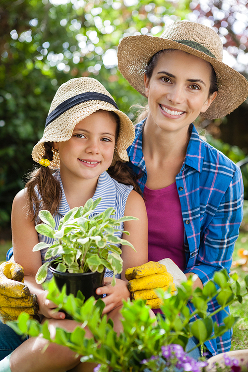 Portrait of smiling mother and daughter with potted plants gardening in backyard