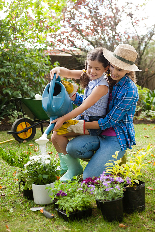 Happy mother teaching daughter to water plants while gardening in backyard