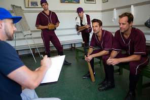 Baseball team planning with coach while sitting on bench at locker room