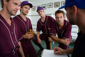 Close up of confident baseball team planning with coach while standing at locker room