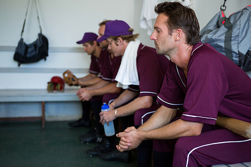 Side view of tired basball players sitting on bench at locker room