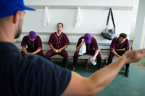 Rear view of coach discussing with baseball team at locker room