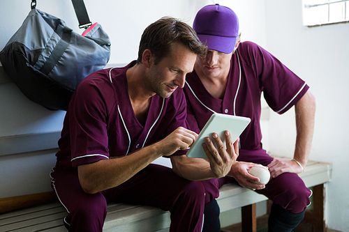 Close up of baseball players using digital tablet while sitting on bench at locker room