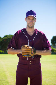 Portrait of confident baseball pitcher standing on field against clear blue sky