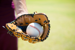 Cropped image of baseball pitcher holding ball on glove at playing field