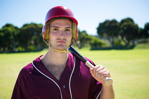 Portrait of young player holding baseball bat while standing on field