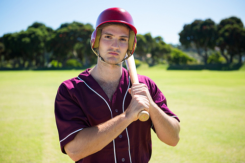 Portrait of young baseball player holding bat while standing on field