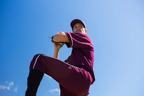 Low angle view of baseball pitcher throwing ball against blue sky on sunny day