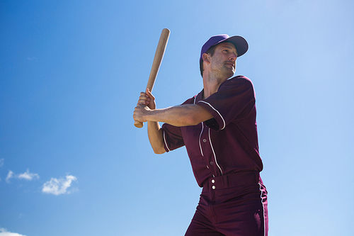 Low angle view of young baseball player holding bat against blue sky on sunny day