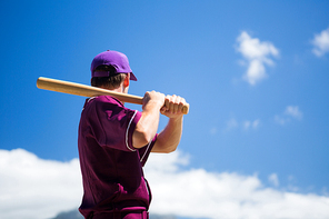 Low angle side view of baseball player holding bat against blue sky on sunny day