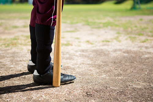 Low section of baseball player holding bat while standing on field during sunny day