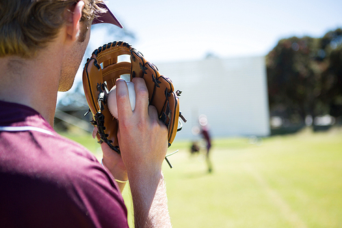 Baseball pitcher holding ball in glove at playing field on sunny day