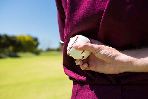 Mid section of baseball player holding ball behind back on sunny day