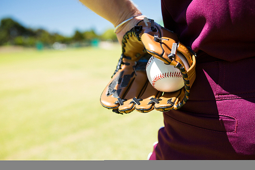 Mid section of baseball pitcher holding ball in glove on sunny day