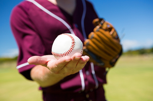 Mid section of baseball pitcher holding ball on palm at playing field