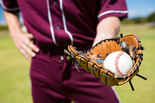 Mid section of baseball pitcher showing ball in glove at playing field