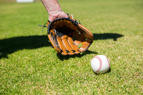 Cropped hand of baseball pitcher by ball on playing field