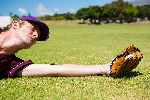 Baseball pitcher catching ball while diving on field during sunny day