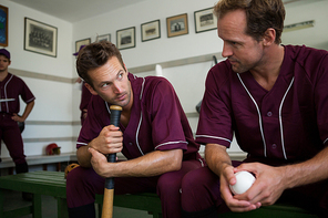 Baseball players sitting together on bench in locker room