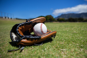Close-up of baseball and glove on grassy field against sky