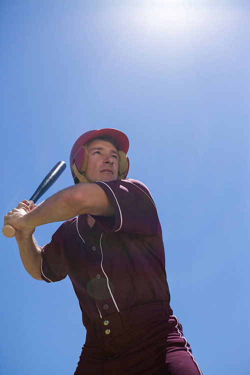 Low angle view of confident player with baseball bat against  blue sky