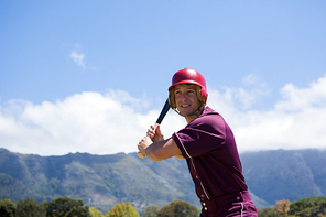 Smiling baseball player with bat standing against mountains