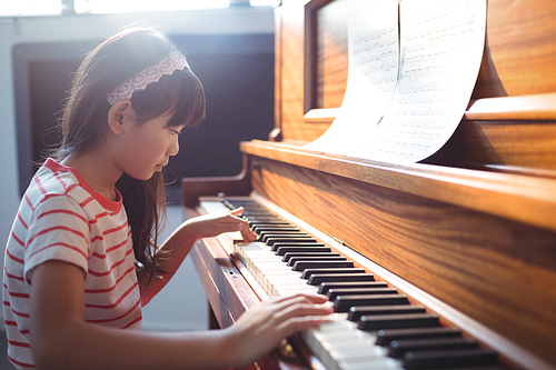 Side view of girl practicing piano in classroom at music school