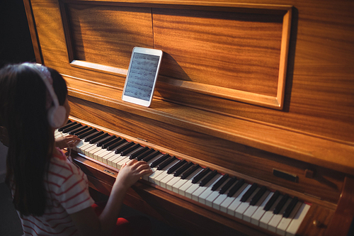 High angle view of girl wearing headphones while practicing piano in classroom at music school