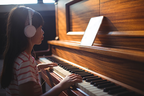 Side view of girl looking at digital tablet while practicing piano in classroom at music school