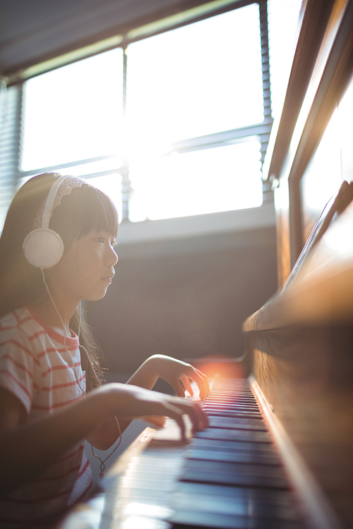 Concentrated girl looking at digital tablet while practicing piano in classroom at music school