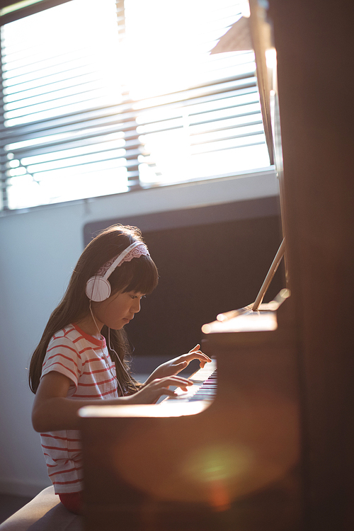 Concentrated girl wearing headphones while practicing piano by window in classroom at music school