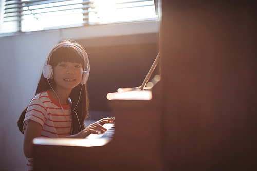 Portrait of smiling girl wearing headphones while practicing piano in classroom at music school