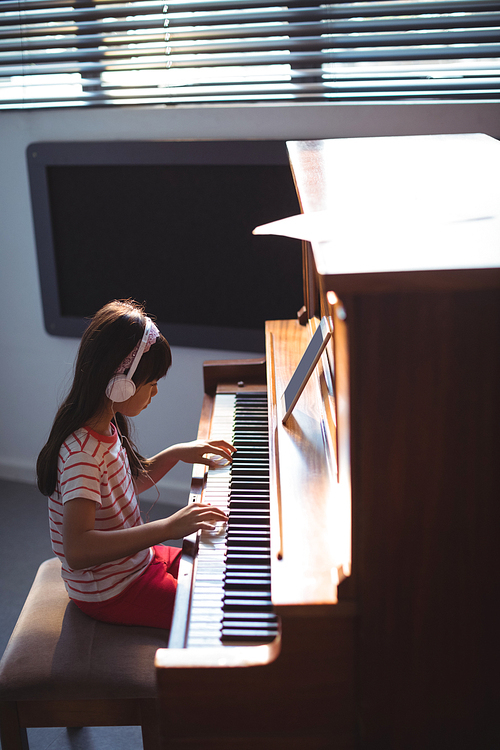 High angle side view of girl wearing headphones while practicing piano in classroom at music school