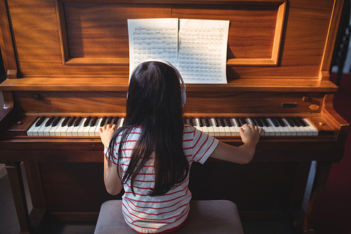 Rear view of girl practicing piano in classroom at music school