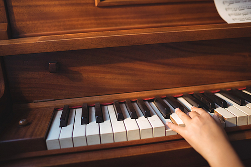 Cropped hand of girl practicing piano in classroom at music school